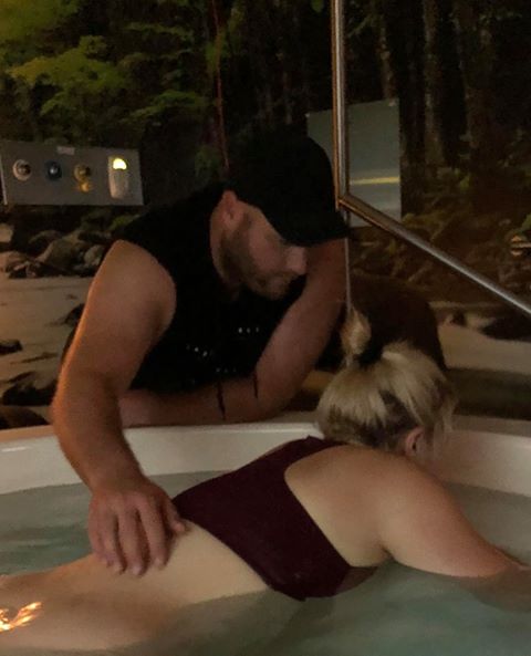 Pregnant mum labouring in birth pool with partner's hand on her back supporting