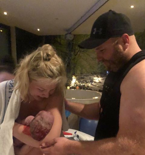 Mum holding newborn baby in her arms and partner by her side arm around her