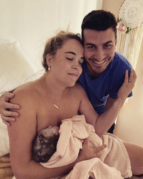 Mum holding baby in her arms with eyes closed and partner with arm around her