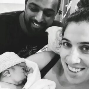 Mum smiling and holding newborn baby in her arms with partner by her side