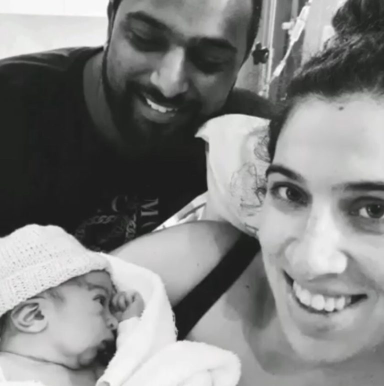 Mum smiling and holding newborn baby in her arms with partner by her side