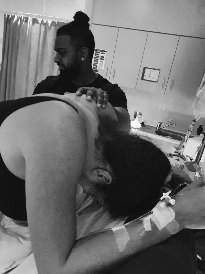 Pregnant mum labouring leaning over bed in hospital with partner near by