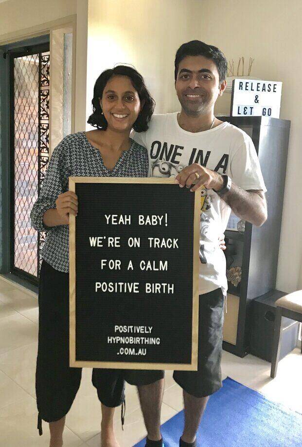 Pregnant couple holding positive birth sign and smiling after doing hypnobirthing class