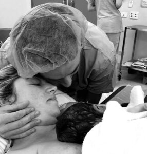 Mum lying down with newborn baby on her chest and partner cuddling them both