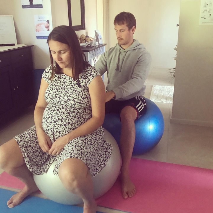 Pregnant mum and partner sitting on a birth ball and partner doing massage on pregnant mum