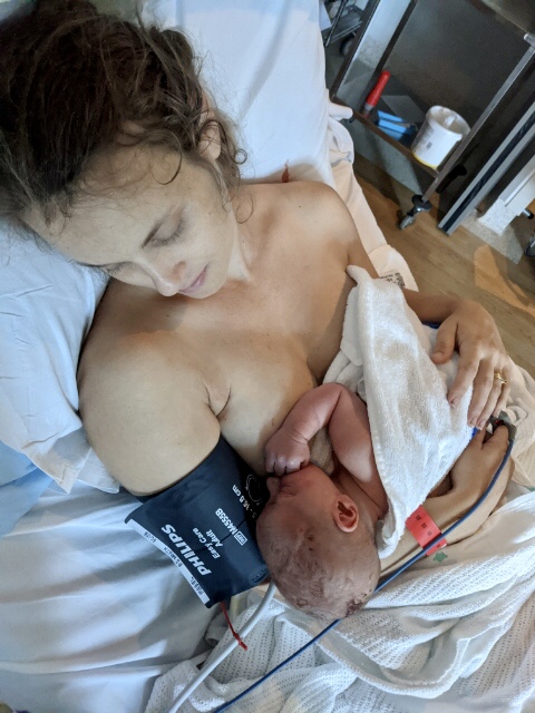 Mum lying on hospital bed with newborn baby in her arms skin to skin 