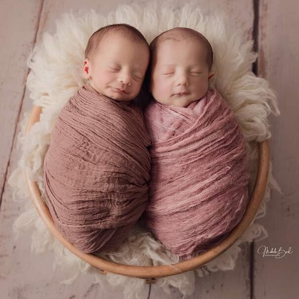 Twin babies wrapped up in a basket and smiling