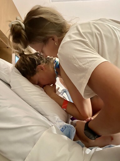 Pregnant mum leaning and labouring on hospital bed with doula by her side supporting