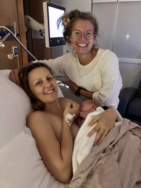 Mum holding newborn baby on her chest skin to skin with her doula by her side