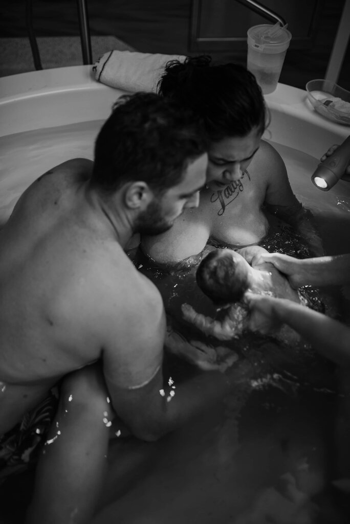 Mum and dad in birth pool after giving birth holding newborn baby