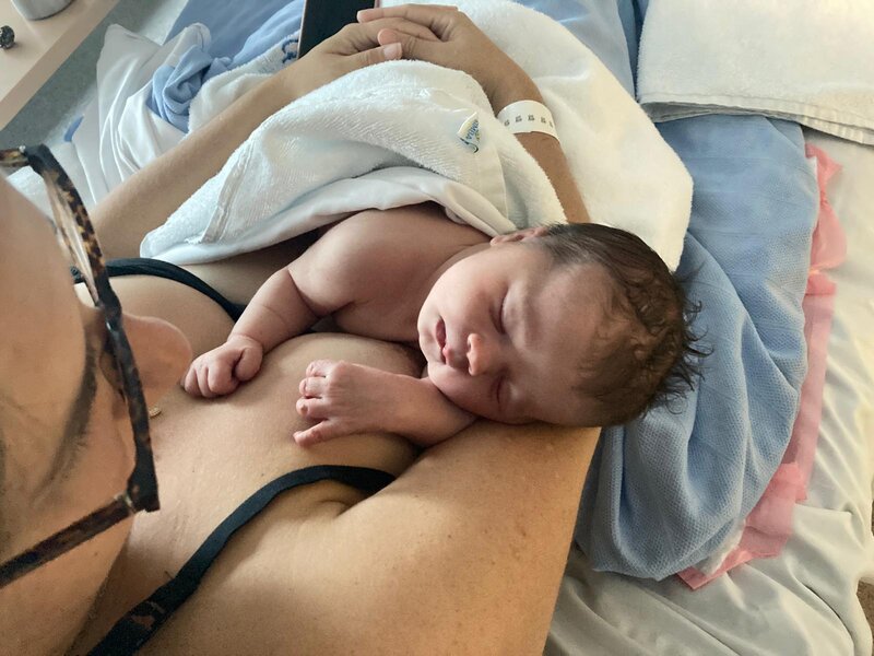 Mum smiling and holding newborn baby skin to skin in hospital