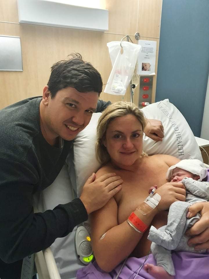 Smiling mum holding newborn baby in hospital bed with partner by her side