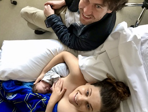 Mum breastfeeding newborn baby in bed with partner by her side