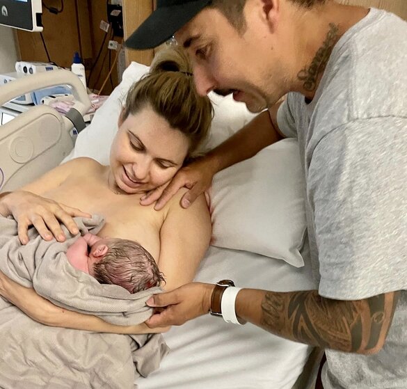 Mum cuddling and looking at newborn baby on her chest with partner by her side