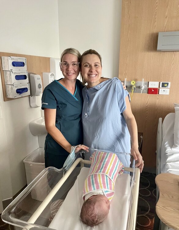 Mum and midwife standing together over newborn baby asleep in bed