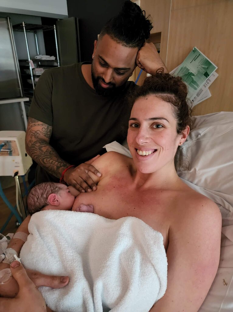 mum holding and breastfeeding baby with partner by her bedside