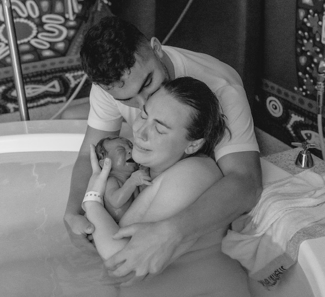 mum in birthing pool holding her newborn baby after birth with her partner cuddling them both