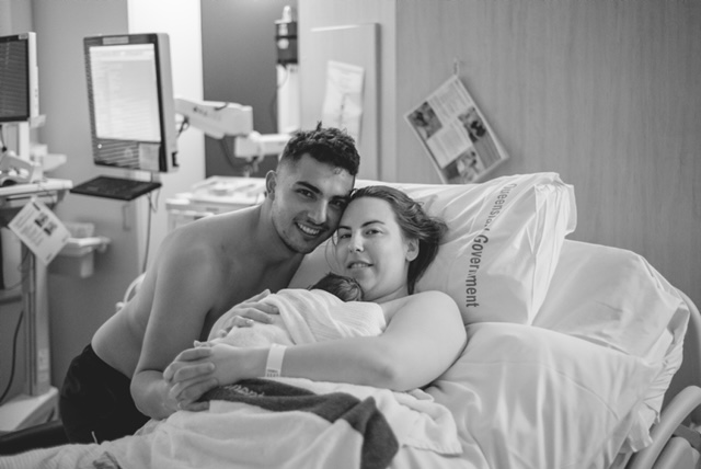 mum on hospital bed holding newborn baby girl with partner by her side