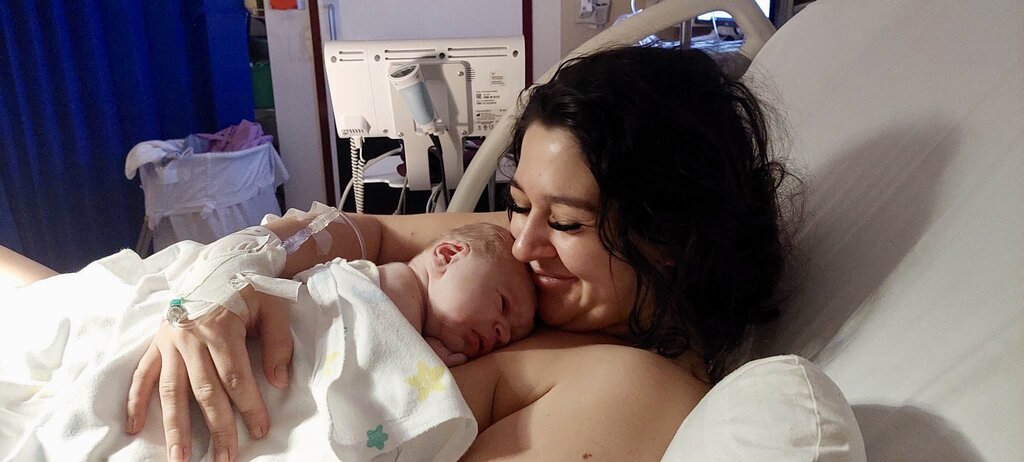 Mum lying in hospital bed holding newborn baby skin to skin smiling