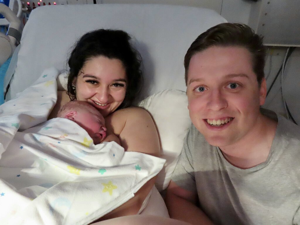 mum holding newborn baby in hospital bed with partner by her side smiling