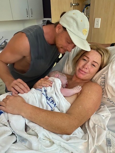 Mum smiling with baby on chest skin to skin and partner by her side