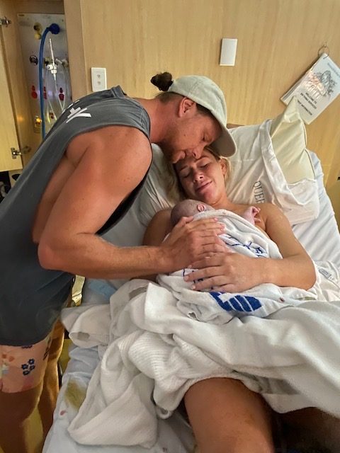 Mum holding newborn baby after birth in hospital bed with partner by her side