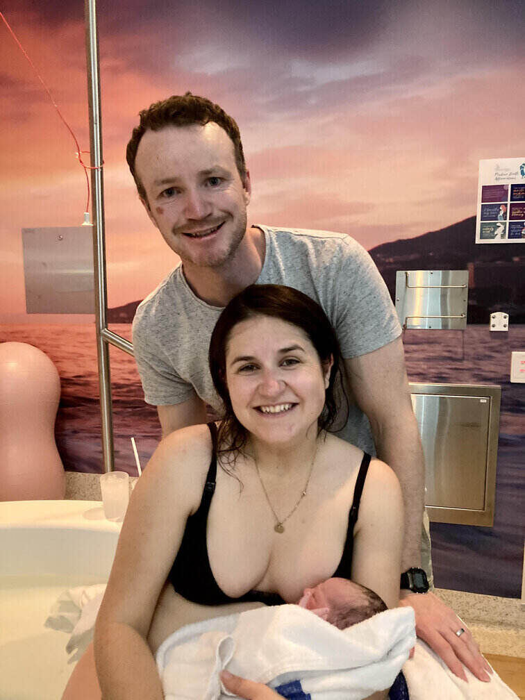 smiling mum in birth pool holding baby with partner behind her
