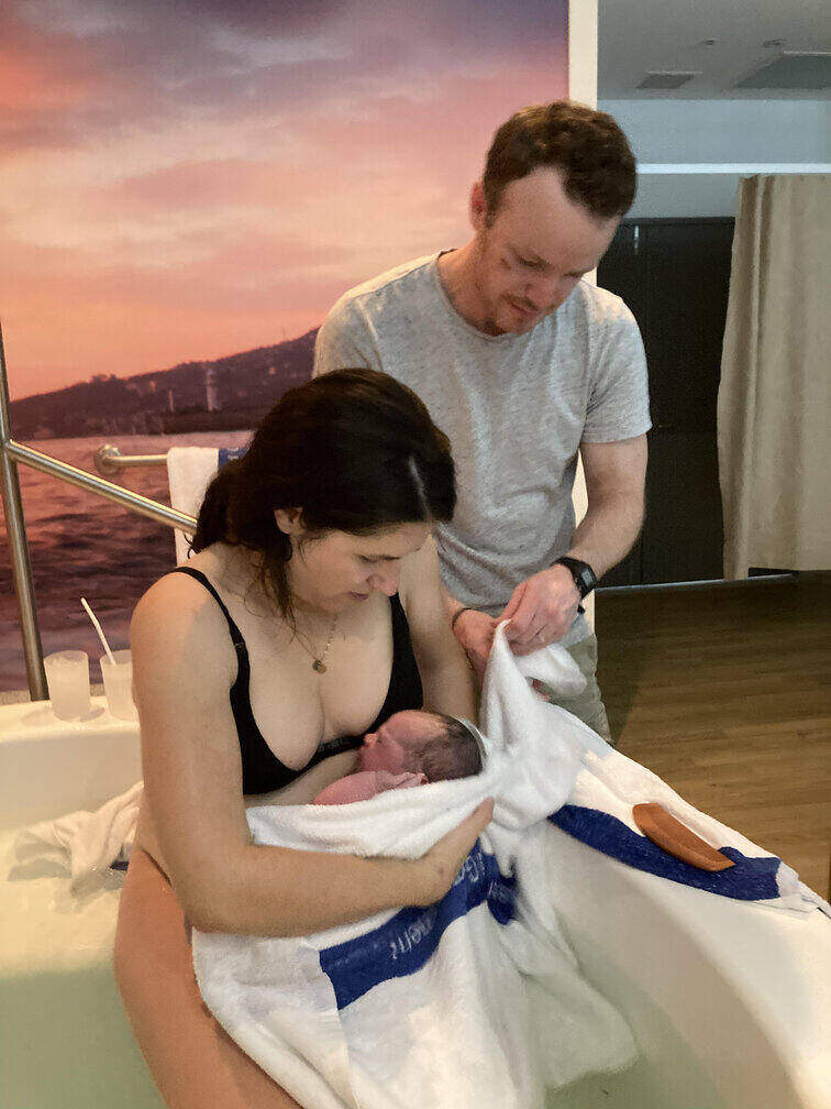 Mum in birth pool wrapping newborn in towel with partner