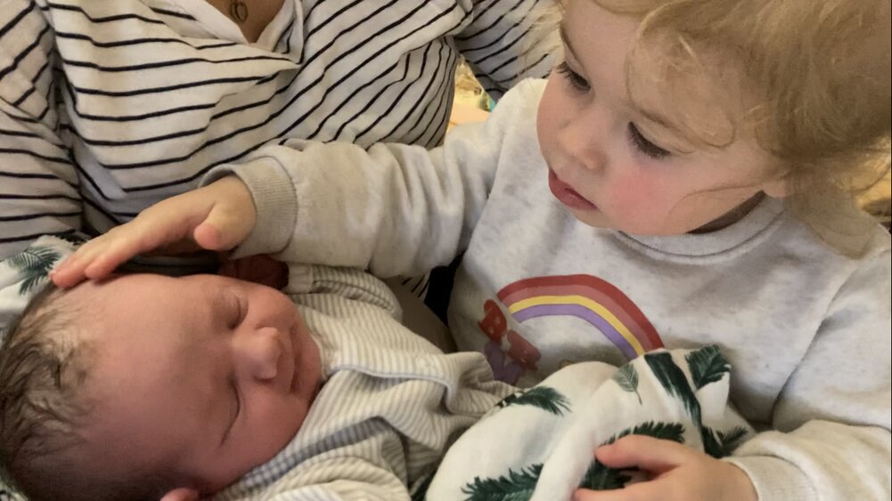sibling patting newborn baby