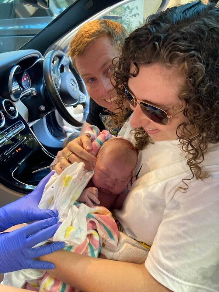 couple holding newborn baby in front seat of car after just birthing