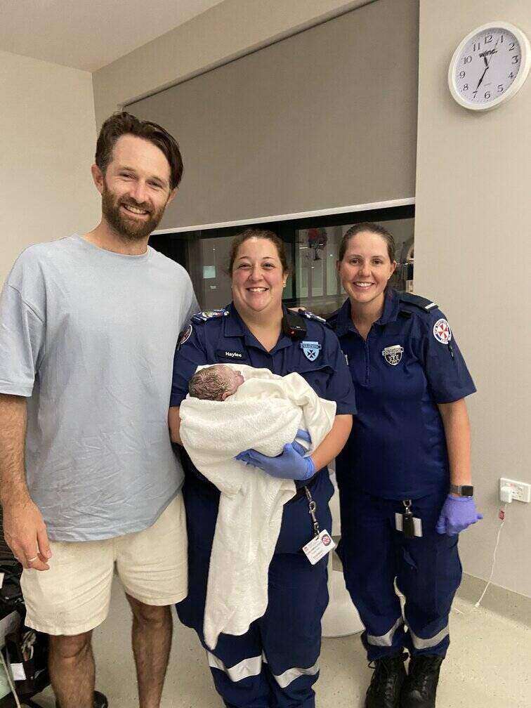 Hypnobirthing dad standing with baby and ambulance staff after mum birthed at home