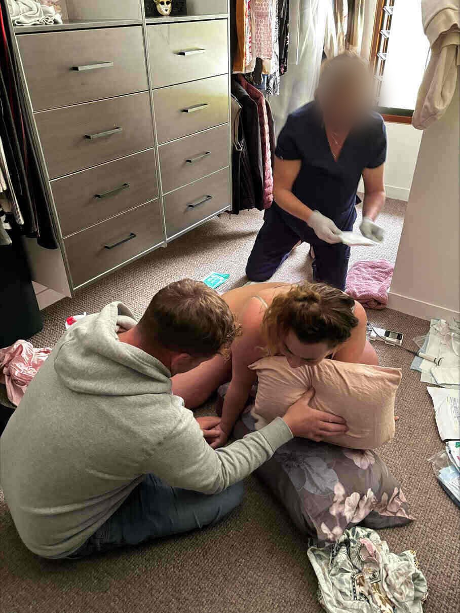 Brooke labouring on hands and knees at home, supported by Joe while her midwife prepares for the birth
