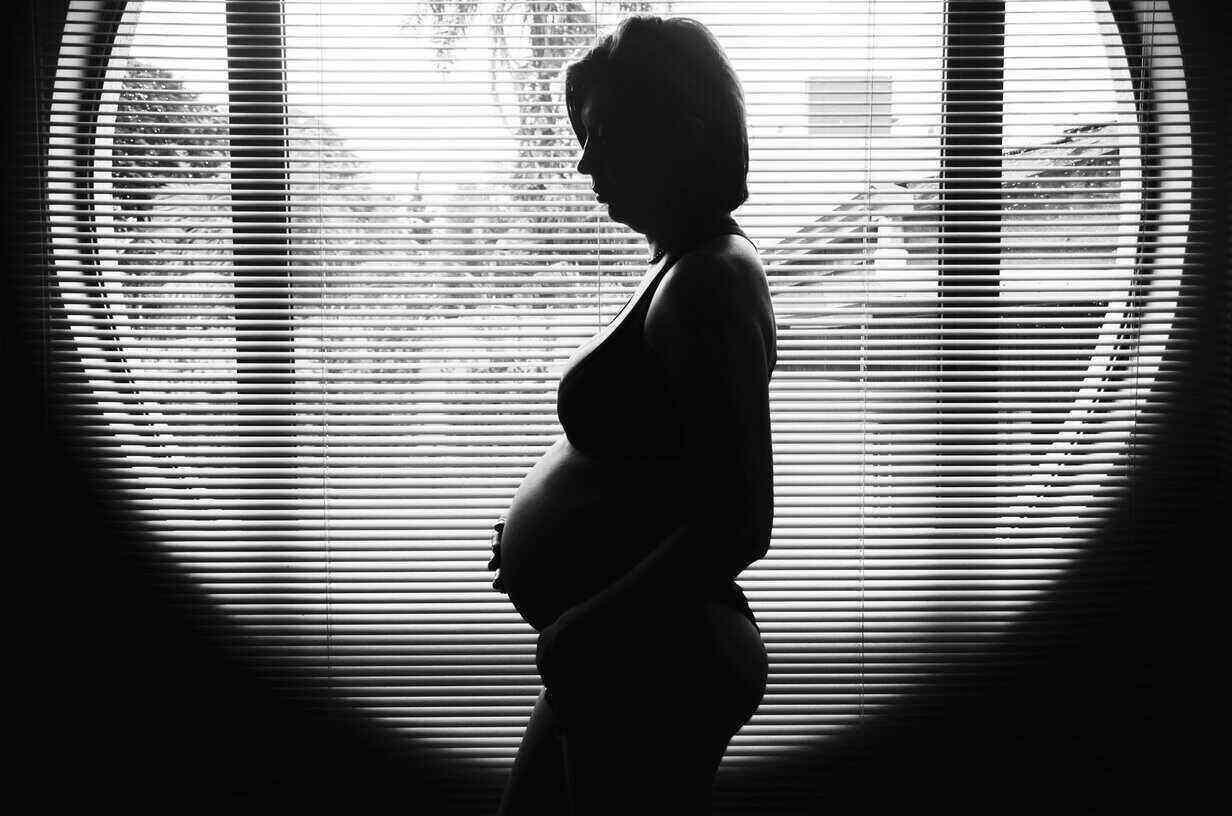 Silhouette of a pregnant mum by a window, waiting calmly for labour to begin