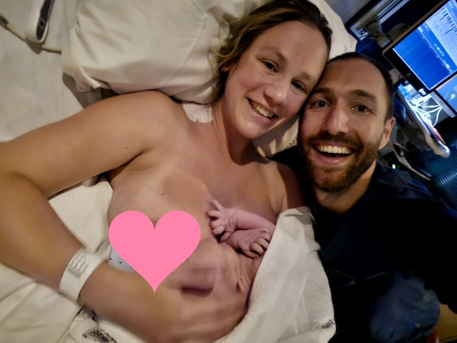 Pregnant couple smiling holding baby in hospital bed after mum births baby